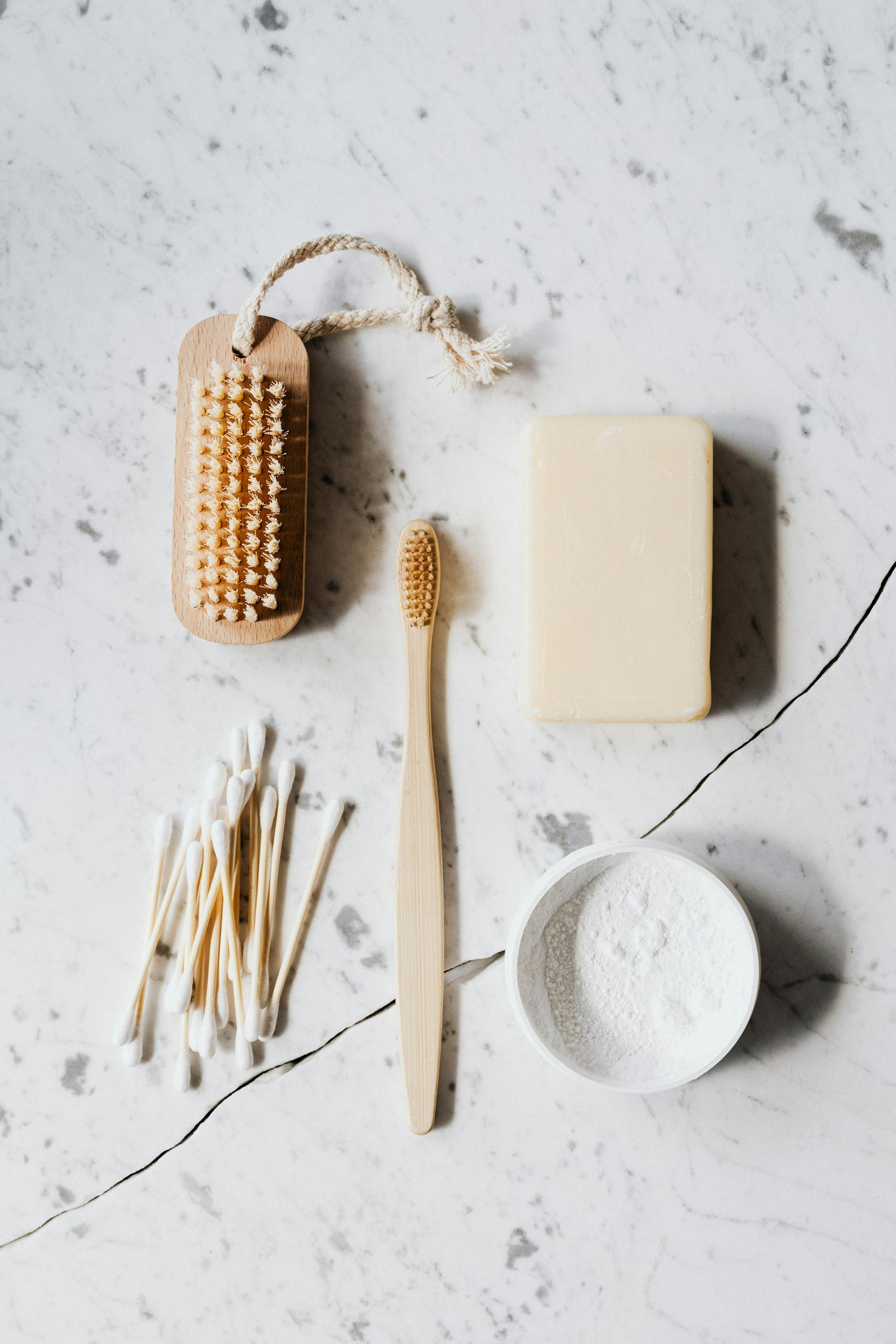 Top view composition of wooden cleaning brush and soap and toothbrush and tooth powder and cotton swab placed on marble surface with line chip